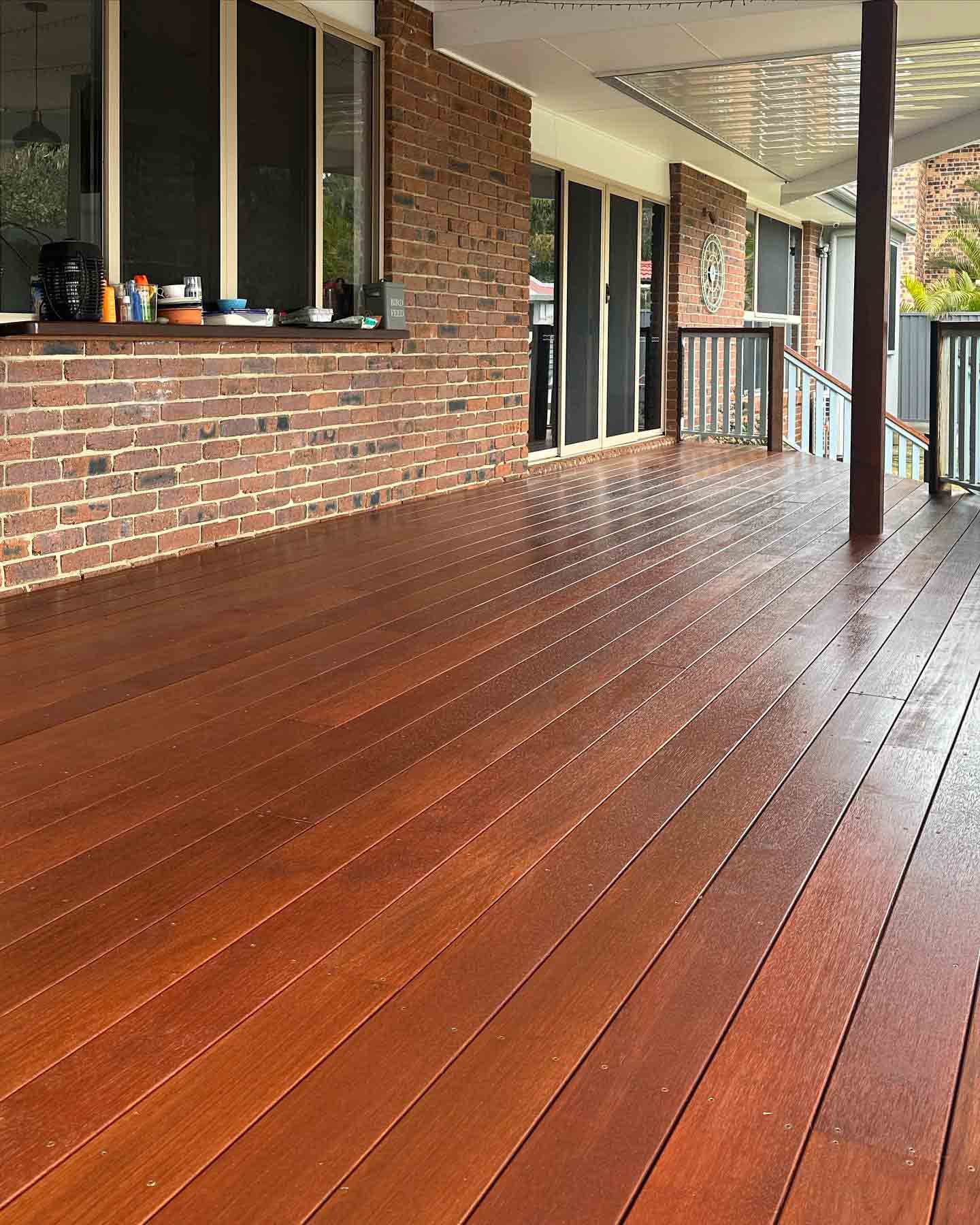 Oiled timber deck under a patio roof along a brick house with a servery window