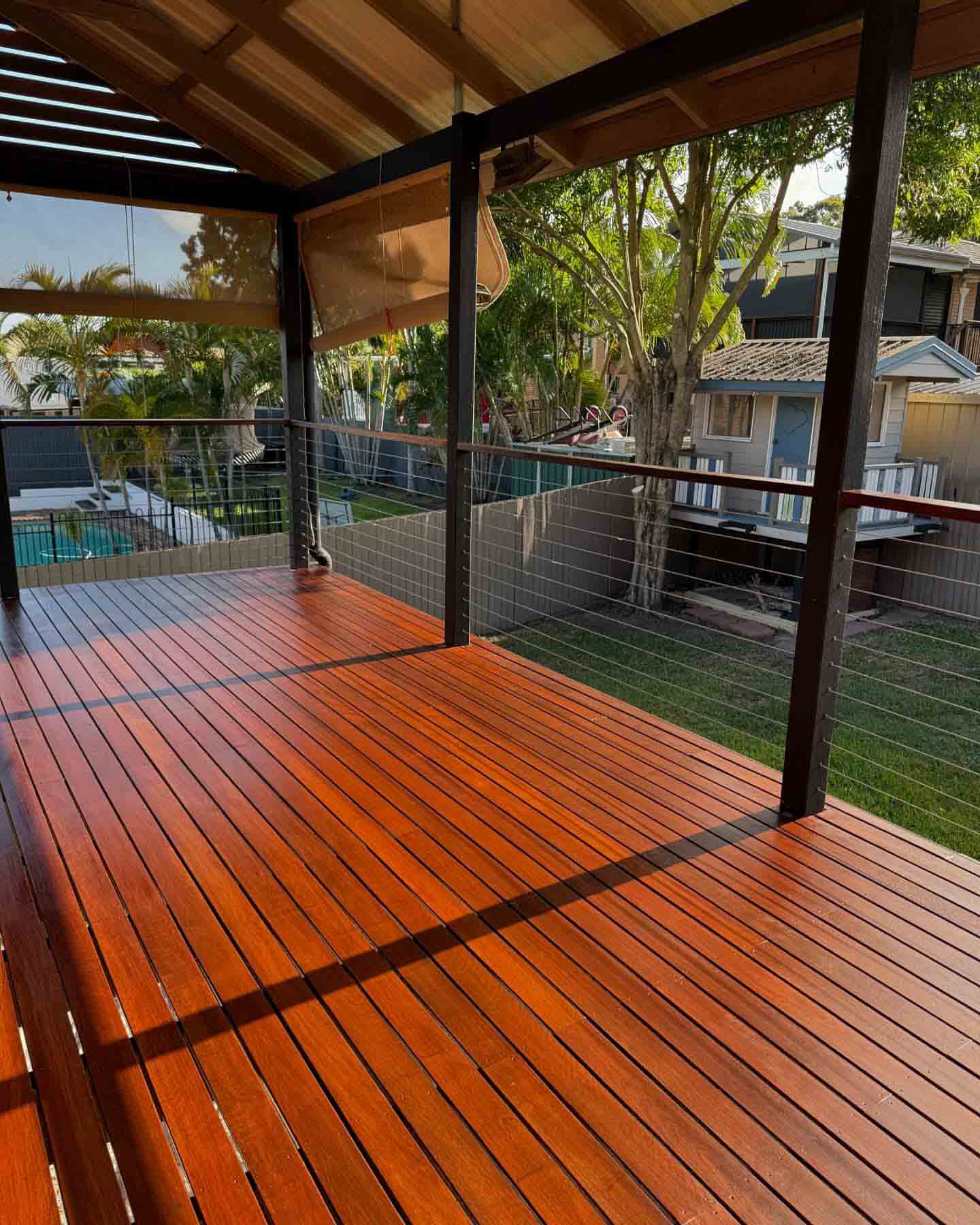 Freshly oiled timber deck with wire balustrade and black posts above a lawn