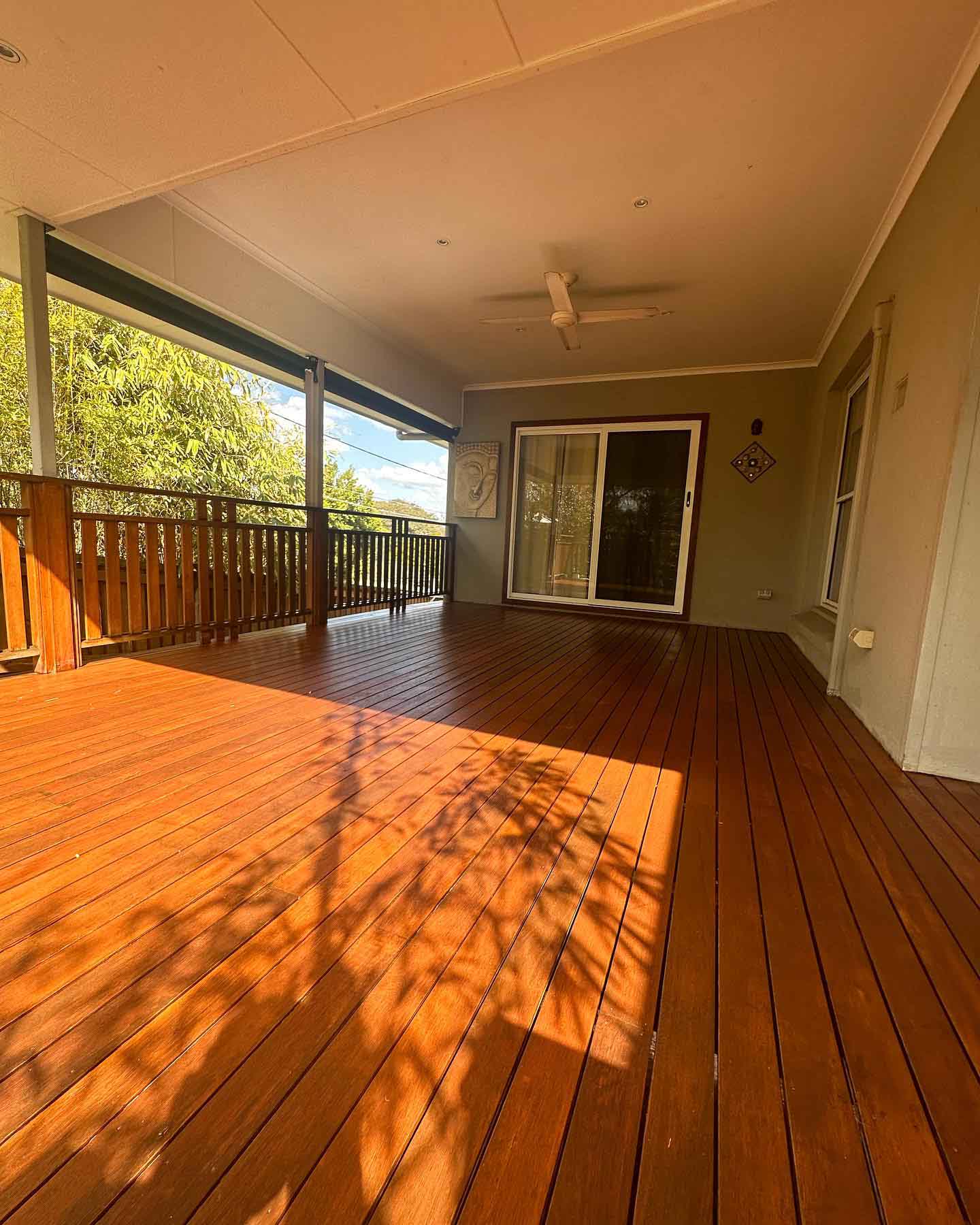 Sunlit oiled timber verandah with timber balustrade under a ceiling fan