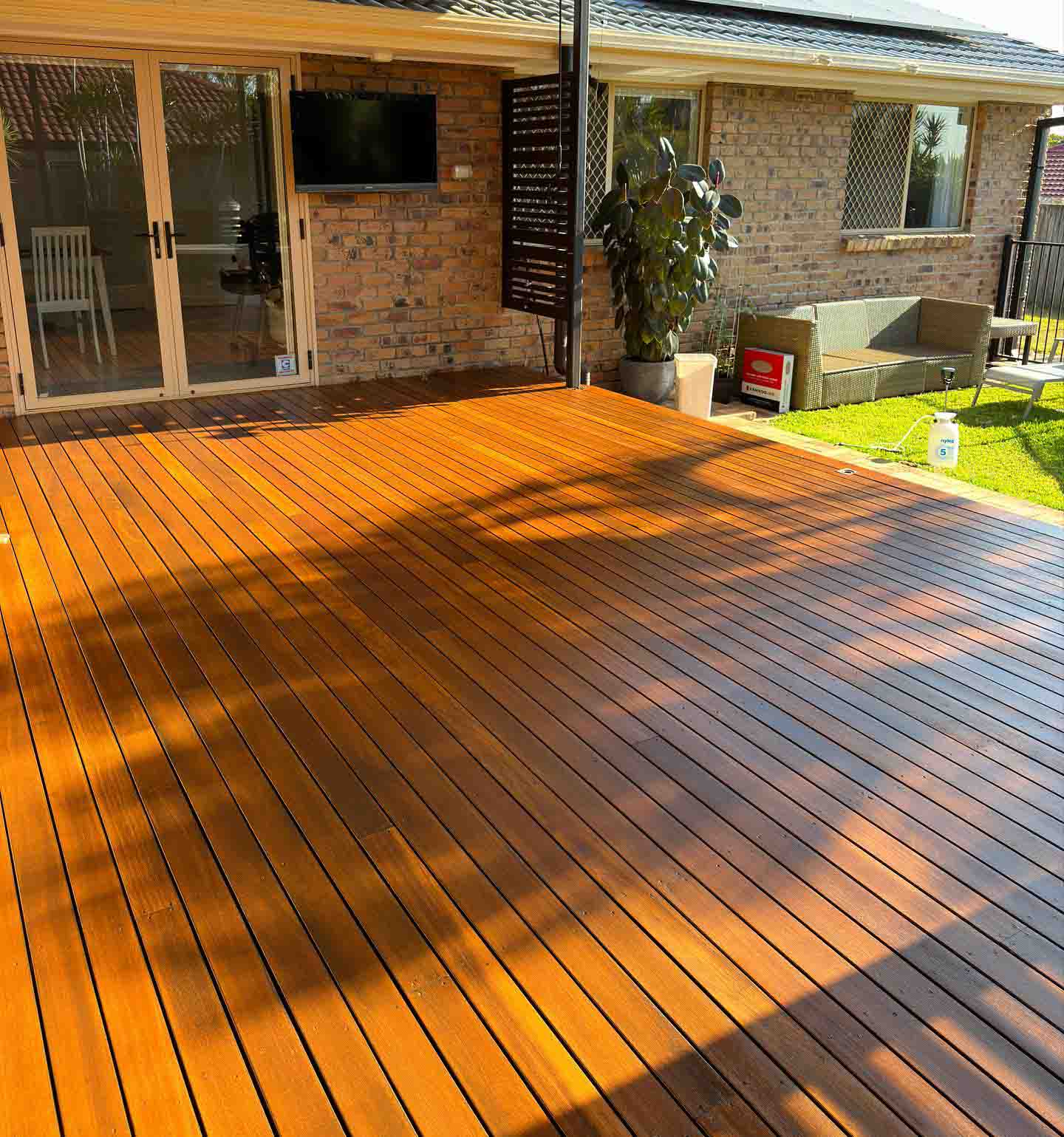 Freshly oiled timber deck in late sun beside a brick house and lawn