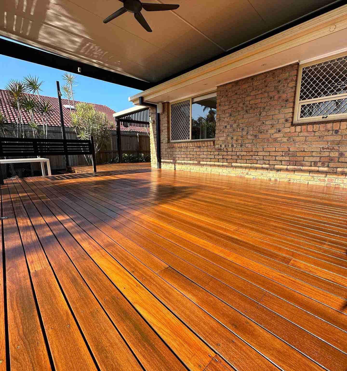 Glossy oiled timber deck under a patio roof against a brick wall, at sunset