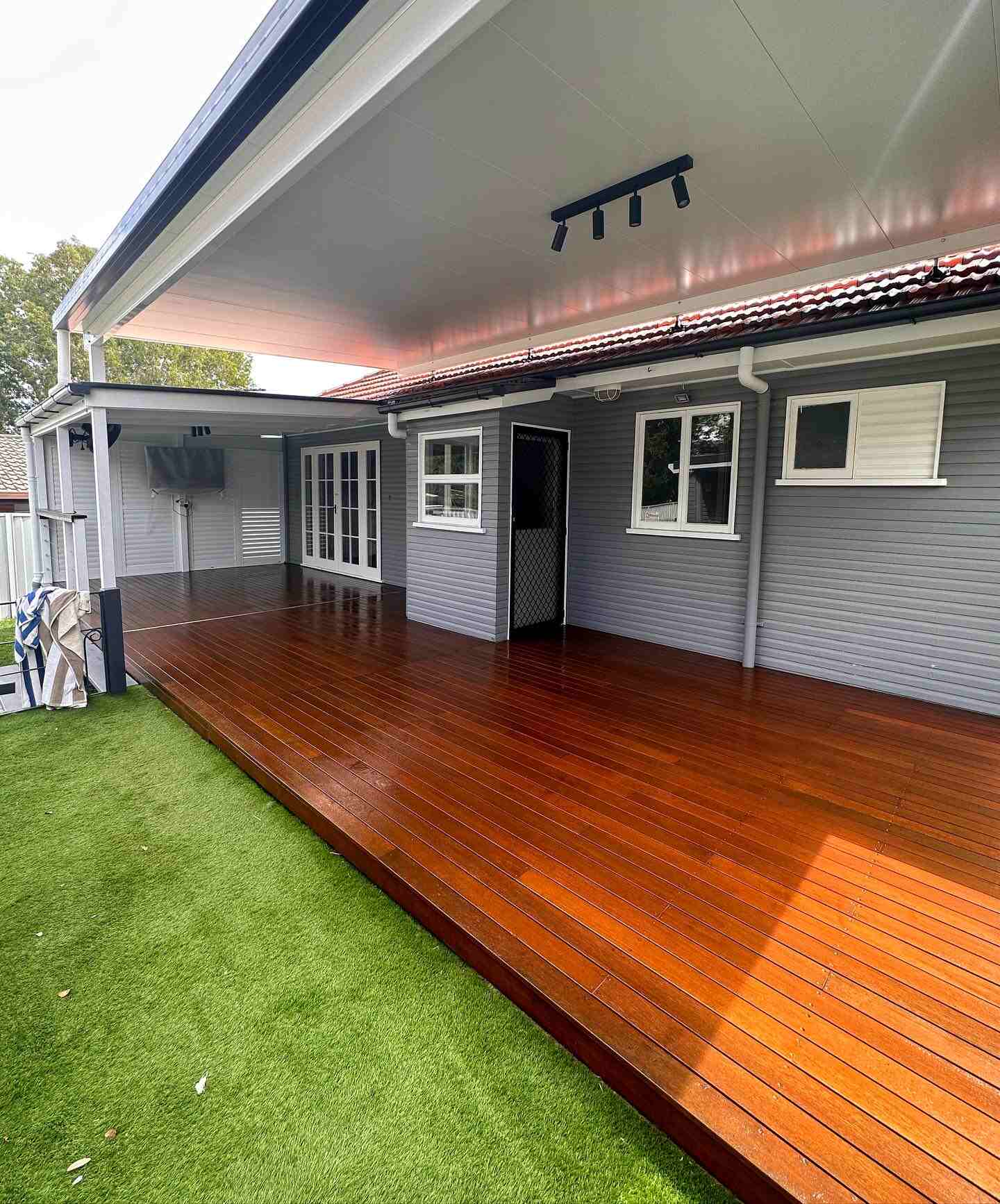 Oiled timber deck along a grey weatherboard house beside artificial turf