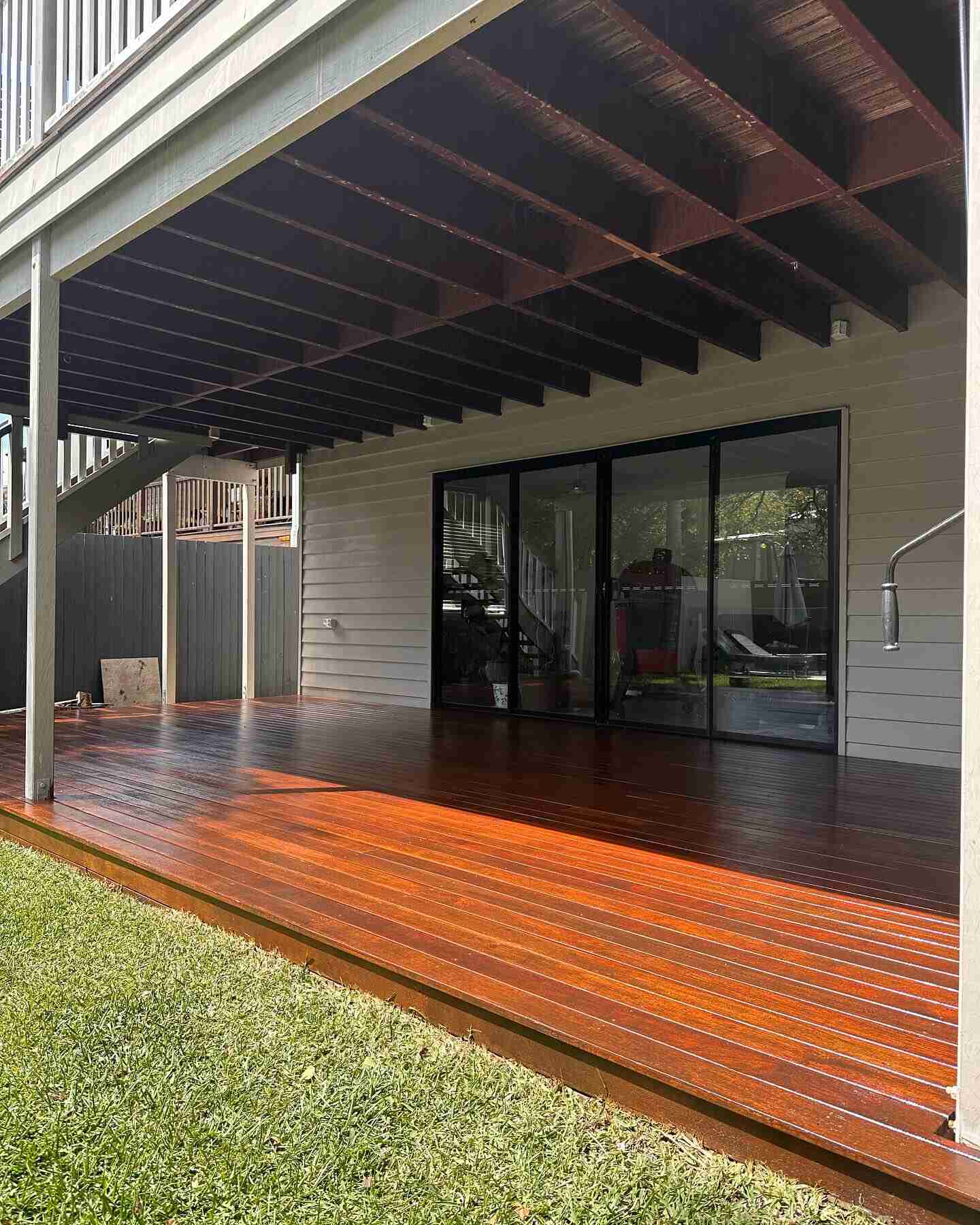 Oiled timber deck under an upper-level deck beside a lawn