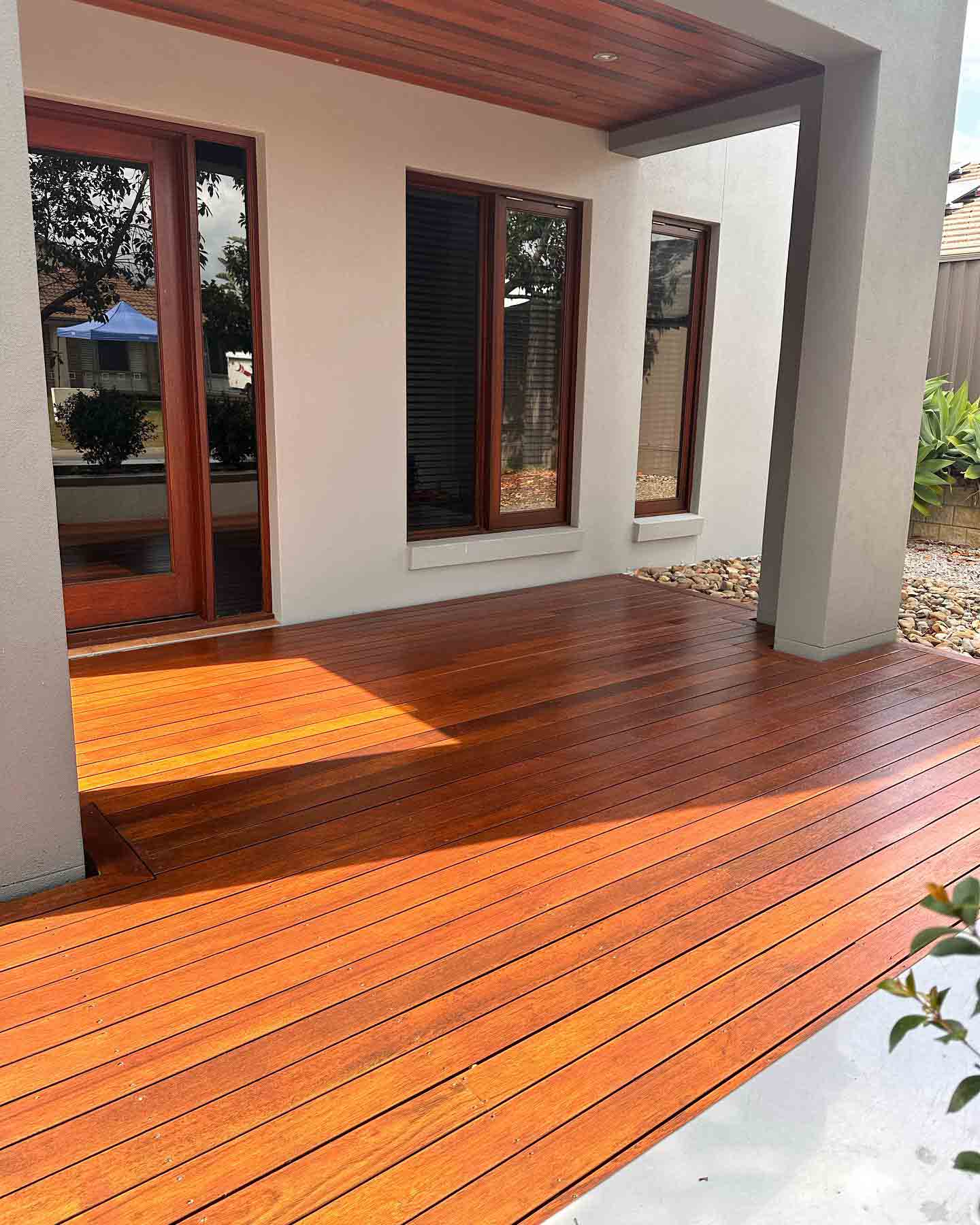 Sunlit oiled timber deck beneath a rendered portico with timber windows