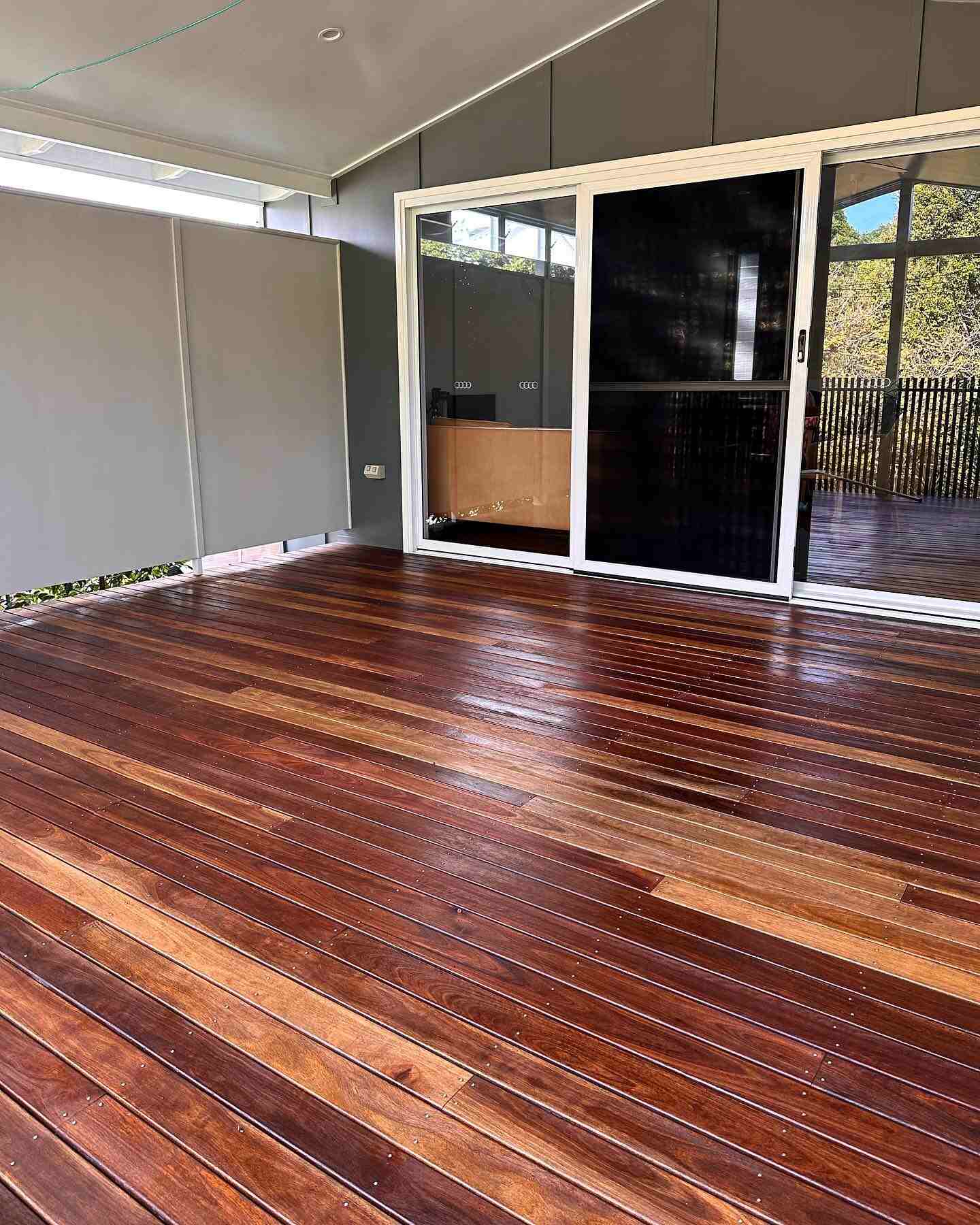 Freshly oiled timber deck with mixed board tones outside black-framed sliding doors