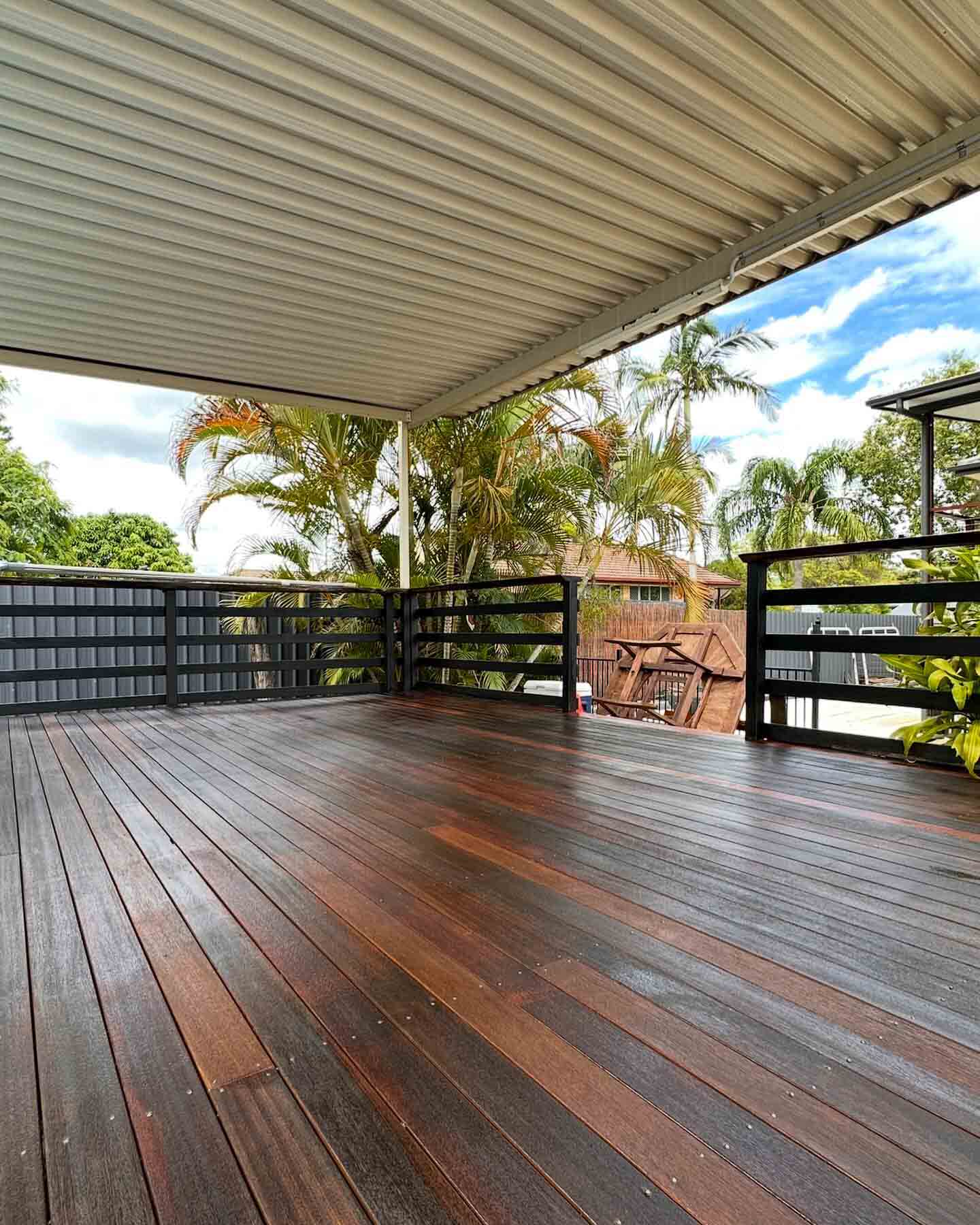 Dark oiled timber deck under a flat roof with black slatted balustrade