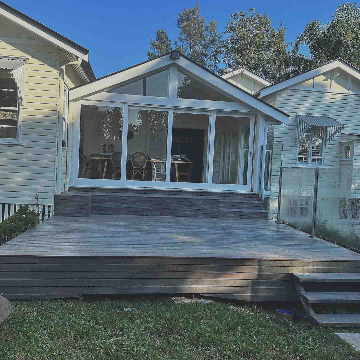Grey-stained deck and steps at the back of a white weatherboard cottage