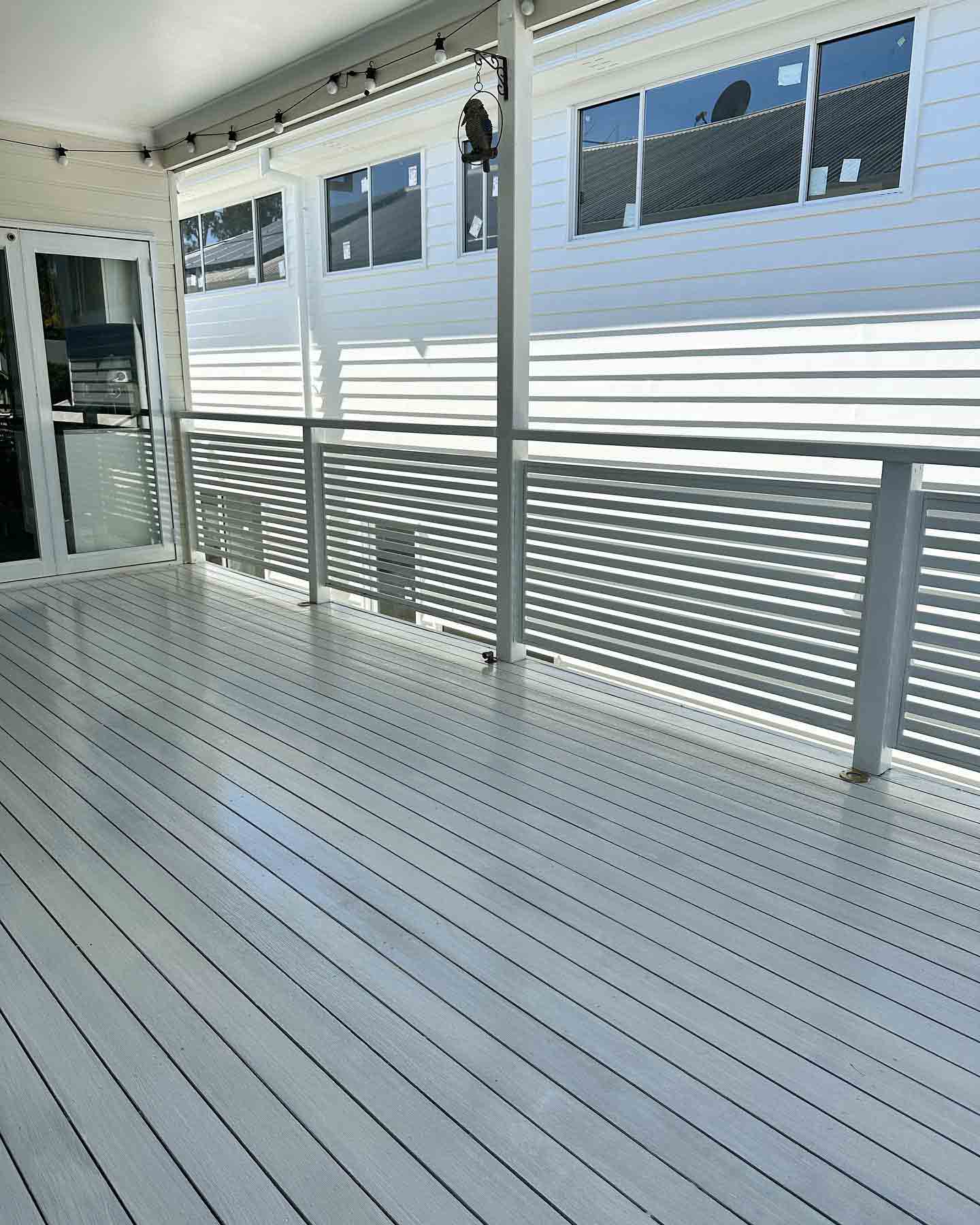 Pale grey coated deck with white slatted balustrade, looking along the house
