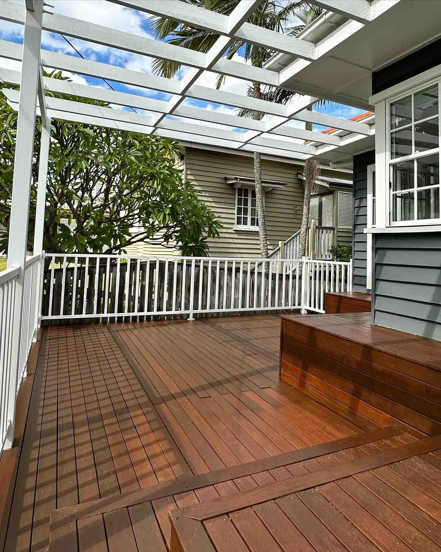 Oiled timber deck with a built-in bench under a white pergola and white balustrade