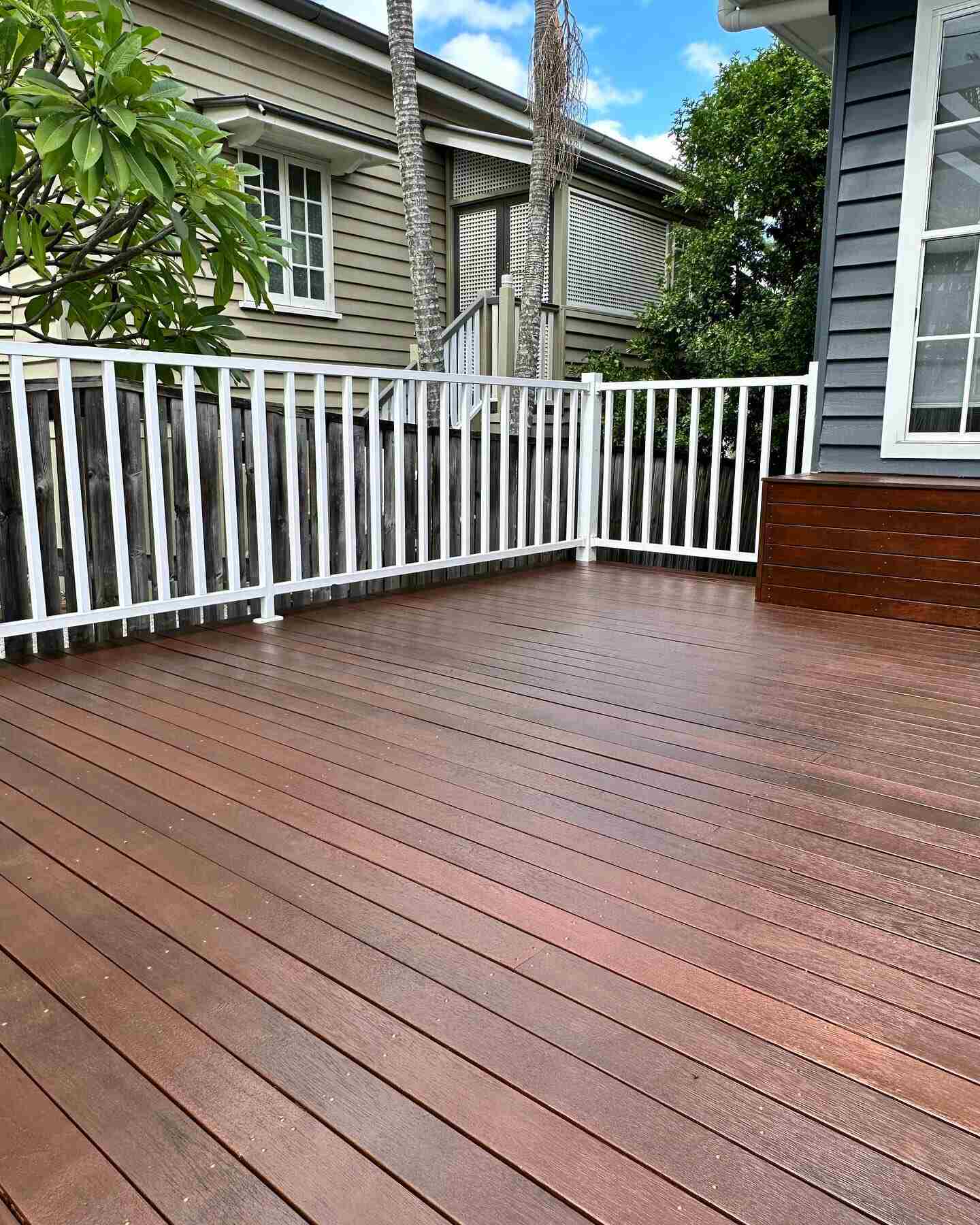 Oiled timber deck with white balustrade beside a grey weatherboard house