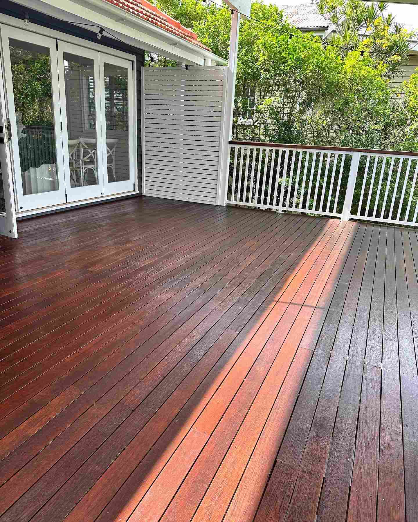 Dark oiled timber deck with white balustrade and a strip of sunlight