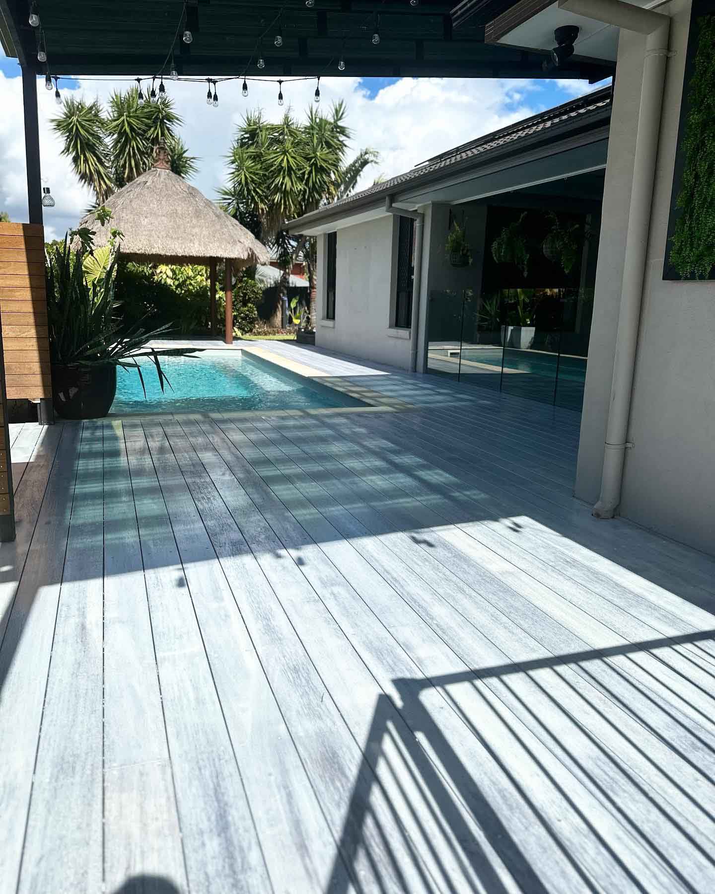 Pale grey deck beside a lap pool with a thatched cabana