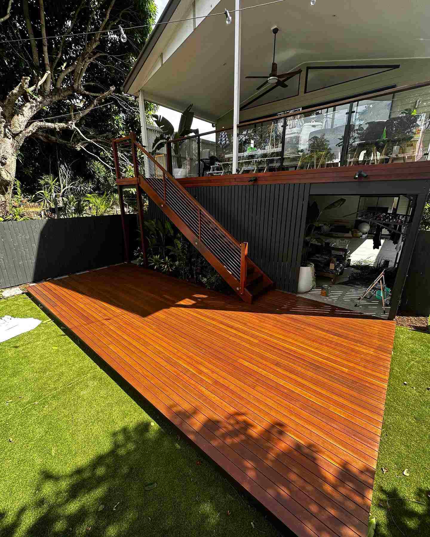 Oiled timber deck on a lawn below an elevated house with timber stairs